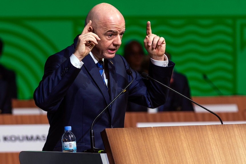 Gianni Infantino gestures with both hands in front of a podium. 