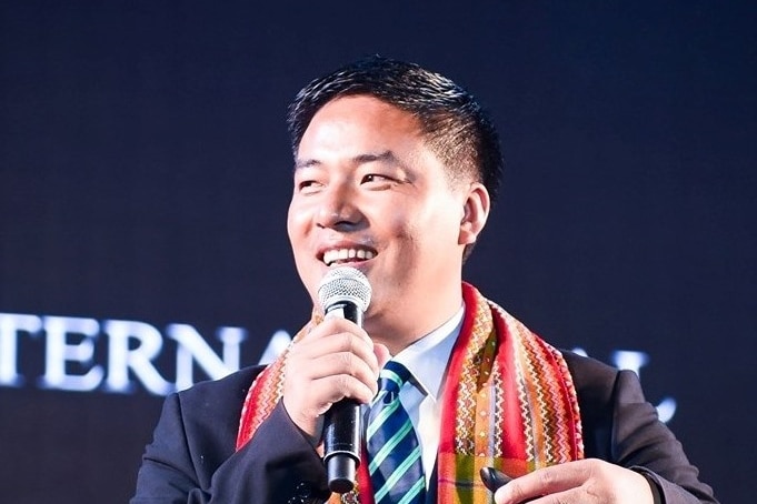 An Asian man in a suit smiling while holding a microphone 