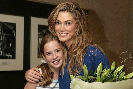 Young girl stands hugging pop star Deltra Goodroom who is holding a bunch of flowers.