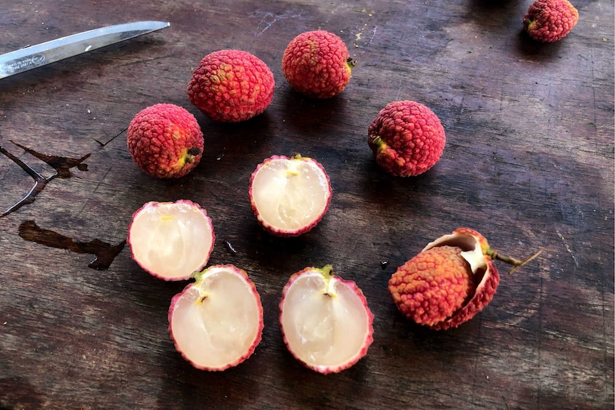 Lychees on a timber bench, some are sliced in half to reveal no seed.