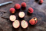 Lychees on a timber bench, some are sliced in half to reveal no seed.