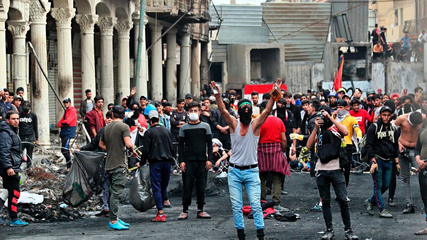 Anti-government protesters gather on Rasheed Street during ongoing protests in Baghdad. Many are masked.