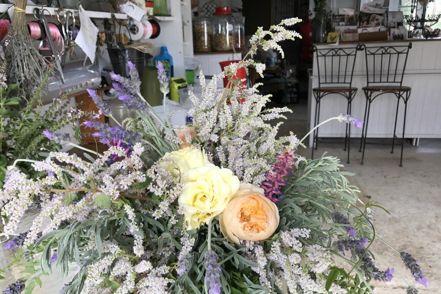 A bouquet of blooms including yellow and peach coloured roses, lavender and basil flowers.