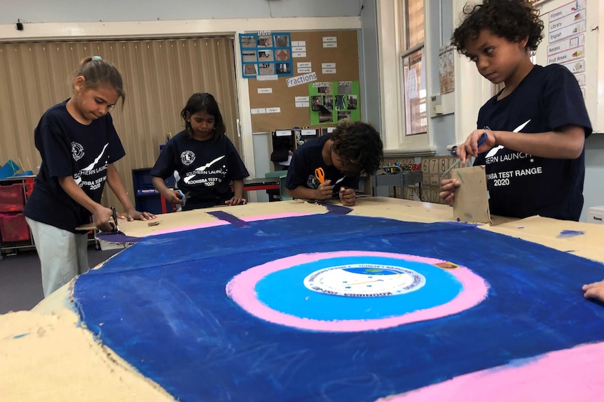 Students painting a piece of cardboard in a classroom