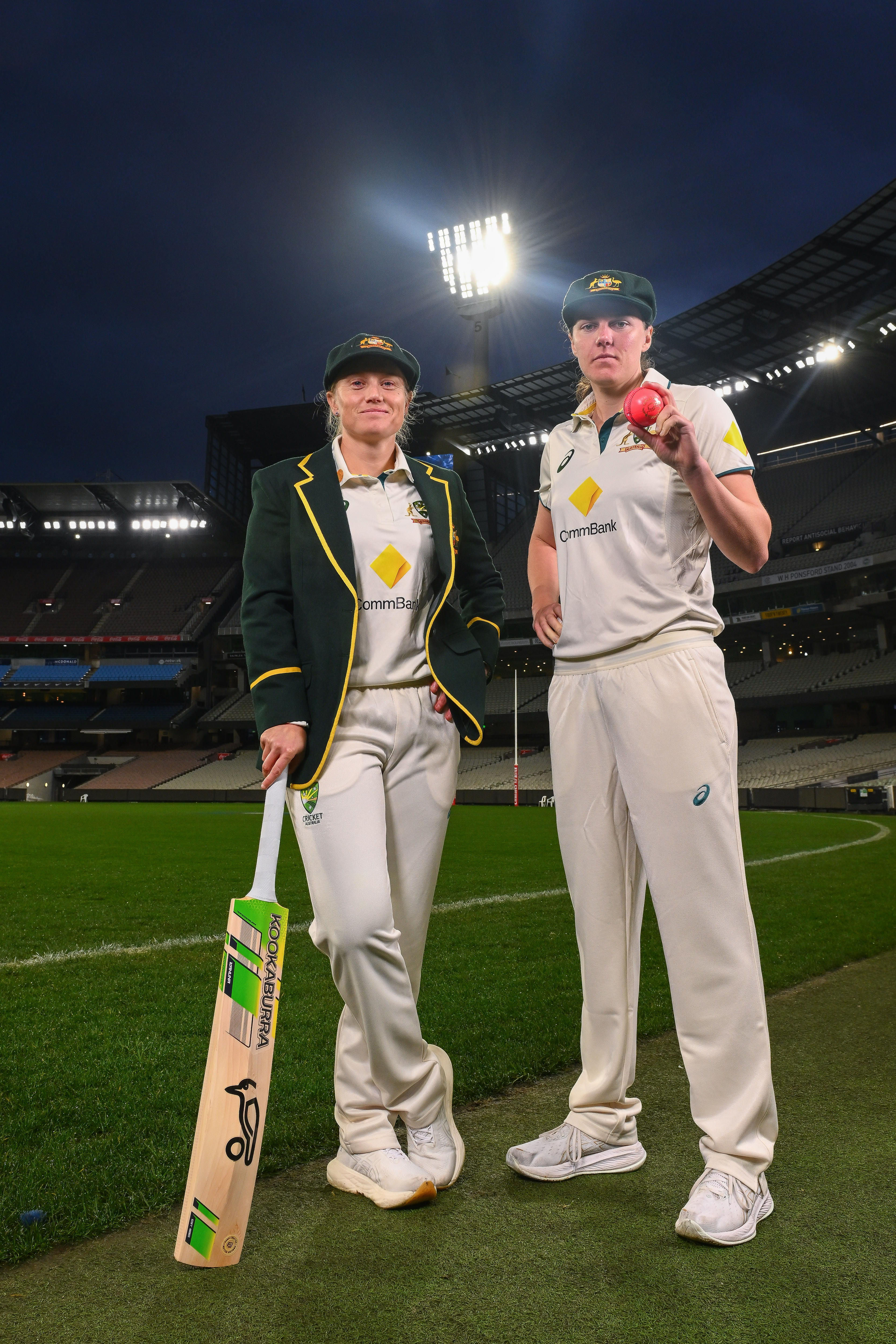 Australia cricketers Alyssa Healy, with a bat, and Tahlia McGrath, with a ball, pose under lights at the MCG.