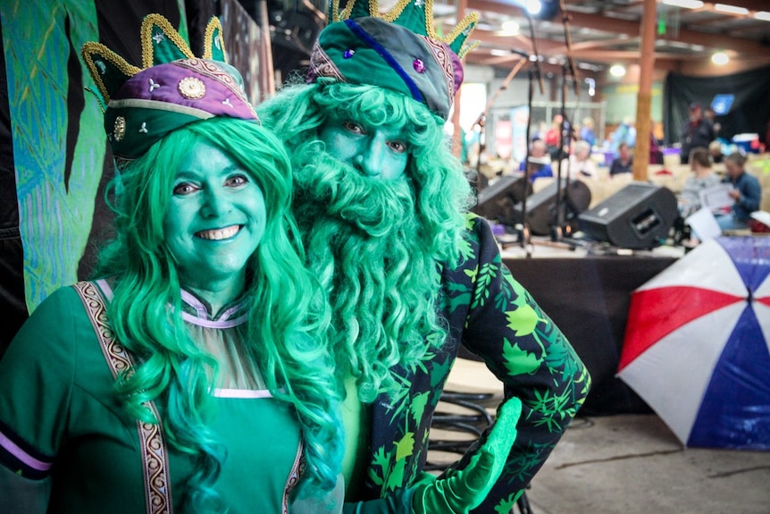 Two street performers, dressed in green, wear regal crowns and robes.