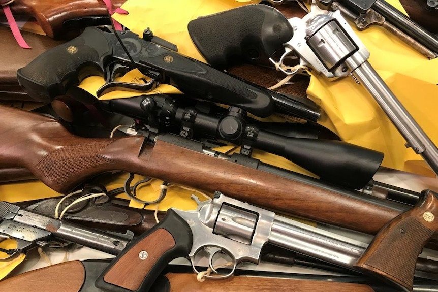 Close-up shot of a range of pistols and rifles on table with yellow labels attached