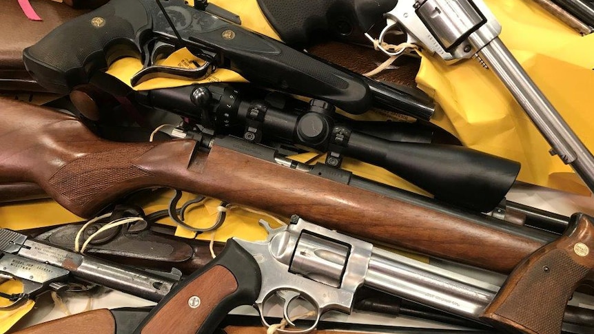 Close-up shot of a range of pistols and rifles on table with yellow labels attached