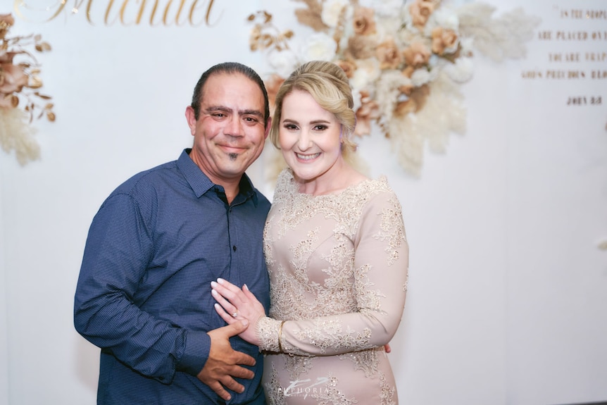 Man in blue shirt hugs woman in white dress