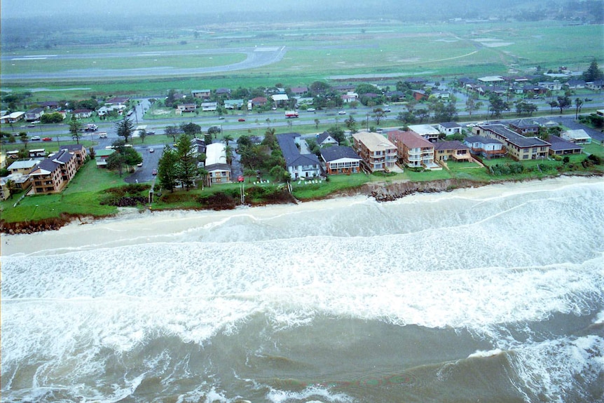Aerial image of coastal erosion by surf near beachfront houses, an airport in the background