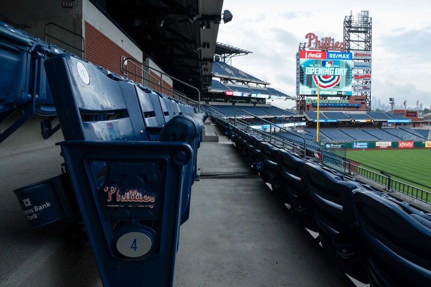 A shot along an empty row of a grandstand in a baseball park, with the scoreboard in the background.