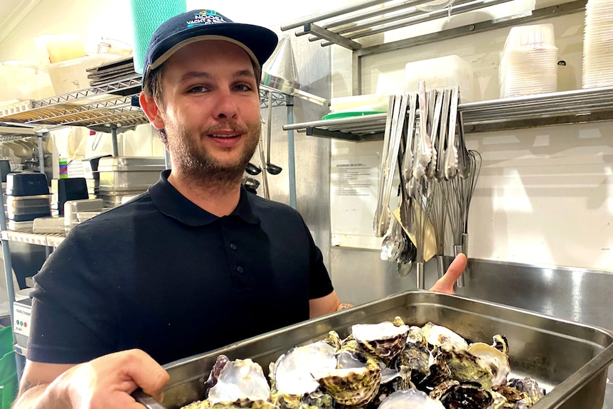 Man wering cap holds tray of oyster shells