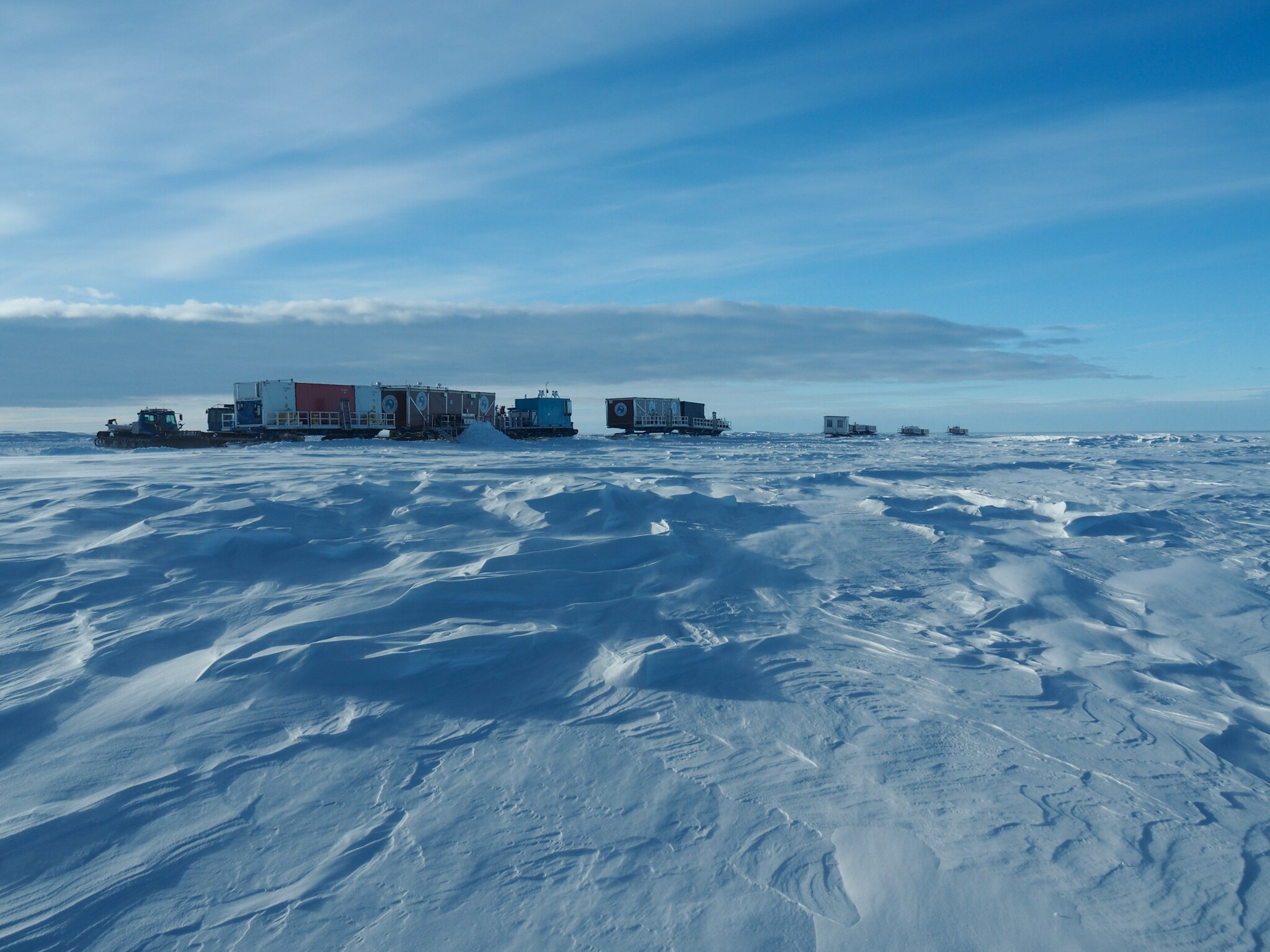 A line of vehicles is seen on the horizon, with vast stretches of snow and ice all around.