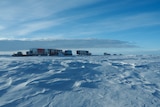 A line of vehicles is seen on the horizon, with vast stretches of snow and ice all around.