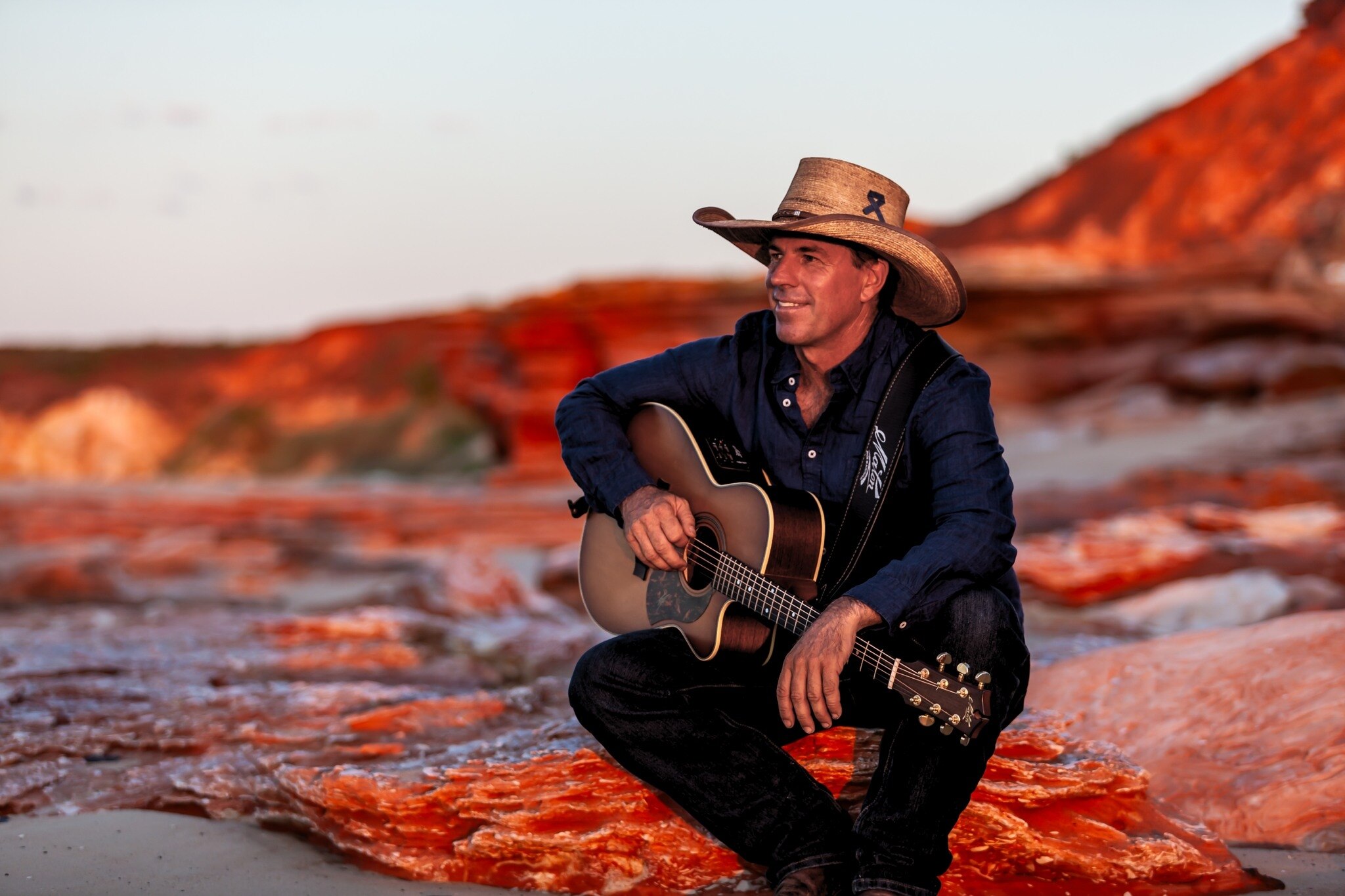 Northern Territory Country singer Tom Curtain sits on a rock in the outback with a guitar