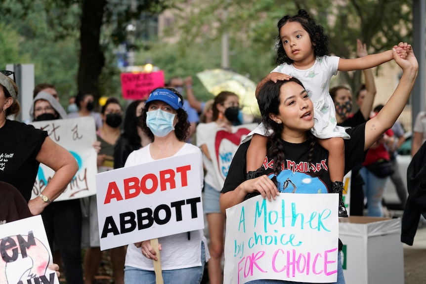 women holding up pro choice signs including a mother with her daughter on her shoulders rally in houston, texas