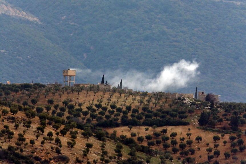 Wide shot of smoke billowing from a building on top of a hill.