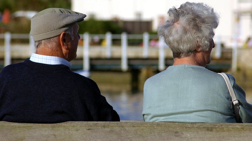 Two pensioners sit side by side on a park bench.