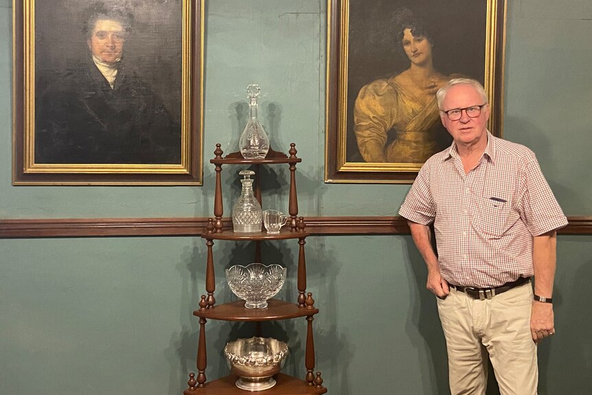 Bruce Tyrrell stands in front of portraits and next to a stand with crystal.