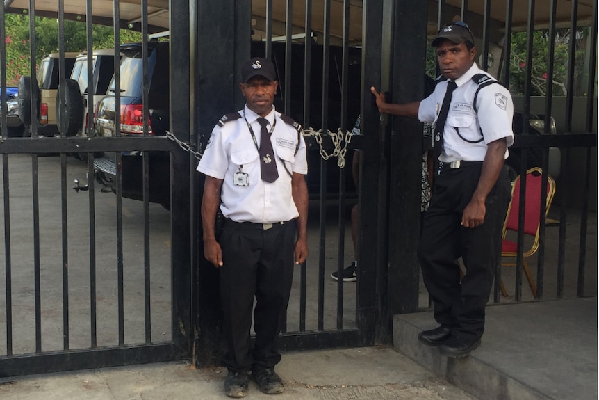 Two security guards stand at a chained up fence
