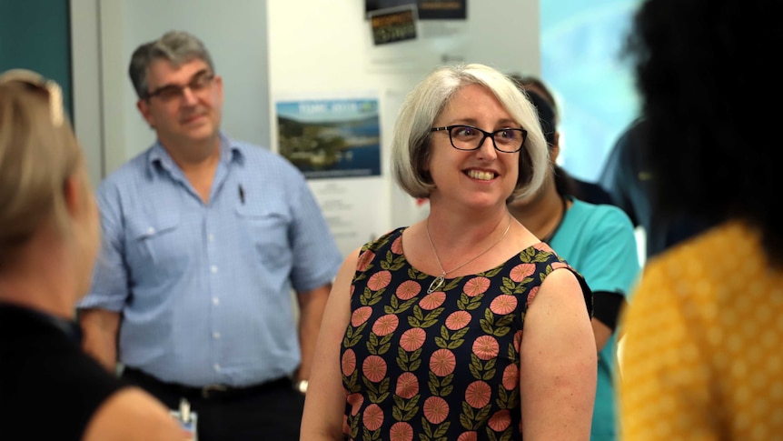 Justine Barwick smiles as she stands at the centre of a group of people.