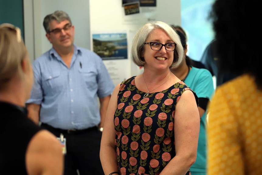 Justine Barwick smiles as she stands at the centre of a group of people.