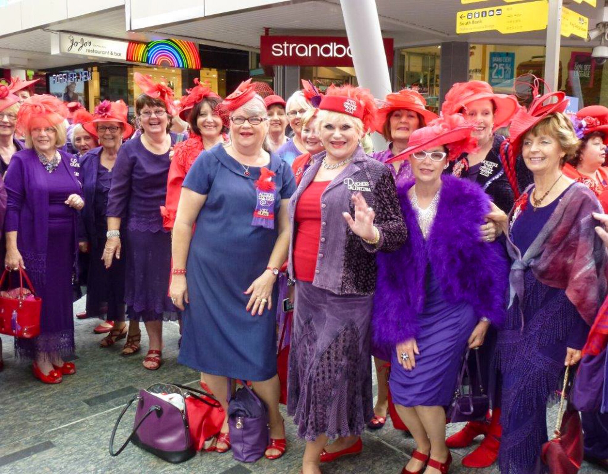A group of women wearing red hats and purple clothes pose for the camera