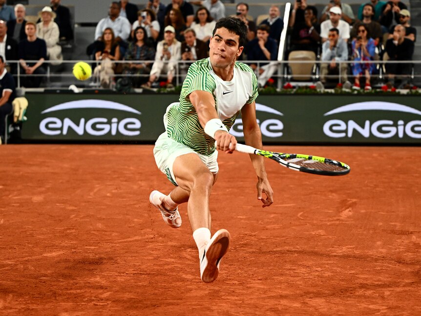 A young Spanish tennis player gets airborne as he slides across the red clay to play a backhand return during a match. 