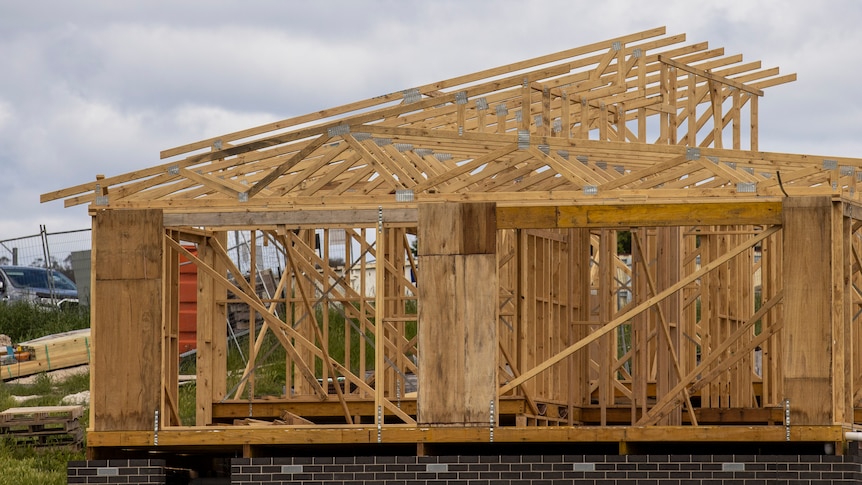 The wooden frame of a house on brown brick foundations on an overcast day