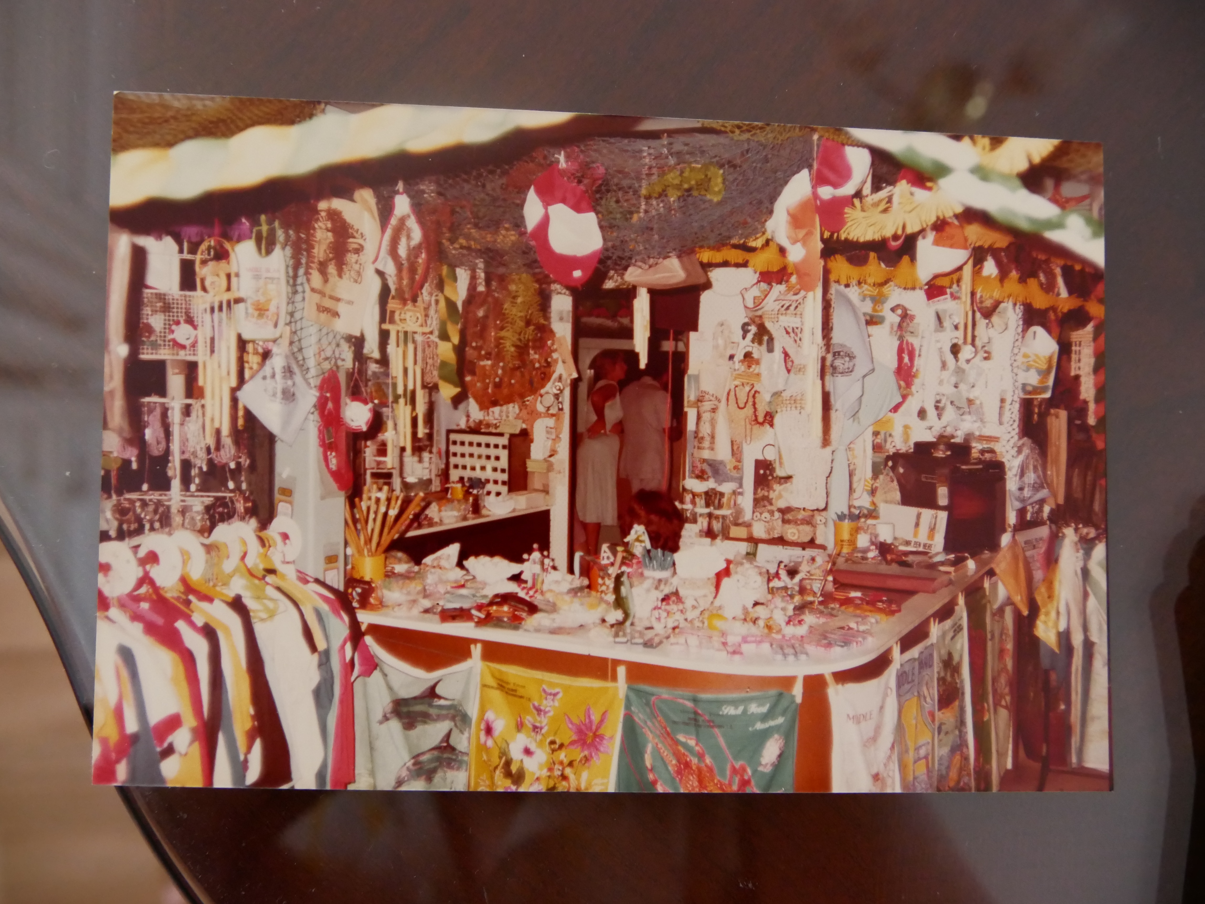 Foto antiga em sépia de uma loja de presentes com toalhas de chá, bugigangas penduradas e pessoas ao fundo