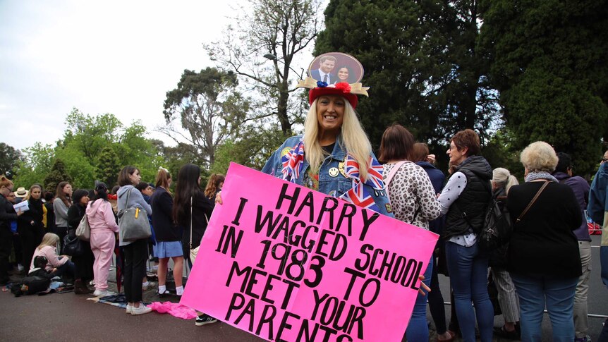 Woman with pink sign reading "Harry I wagged school in 1983 to meet your parents"