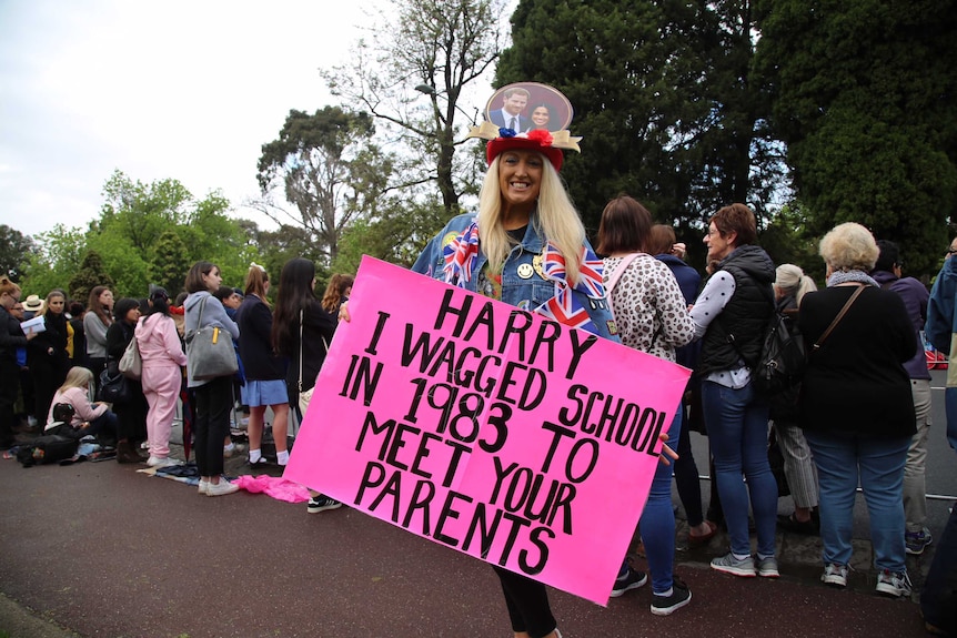 Woman with pink sign reading "Harry I wagged school in 1983 to meet your parents"