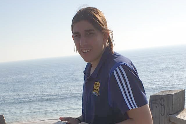 A teenage boy standing near a beach.