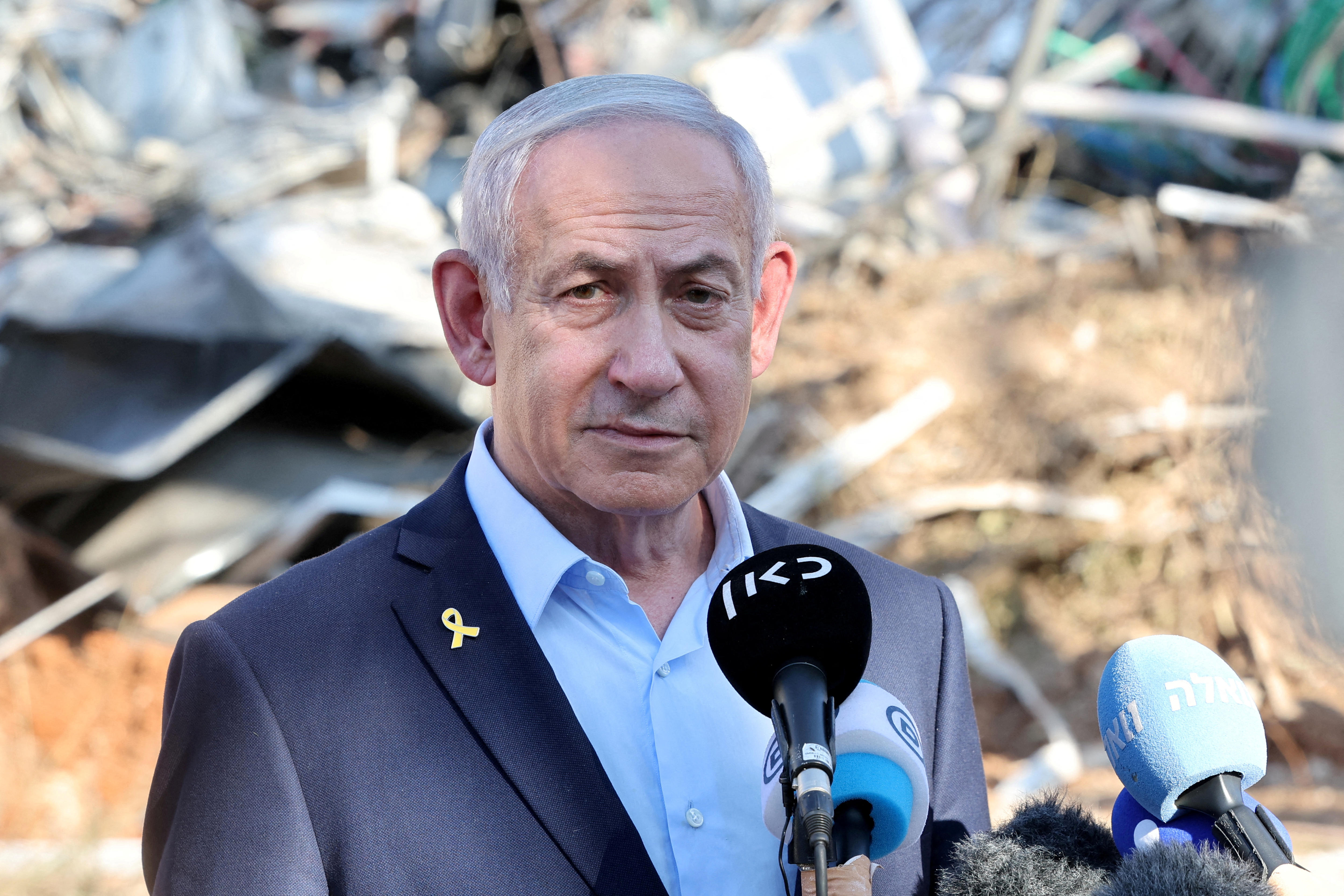 Benjamin Netanyahu standing at a press conference with debris behind him.