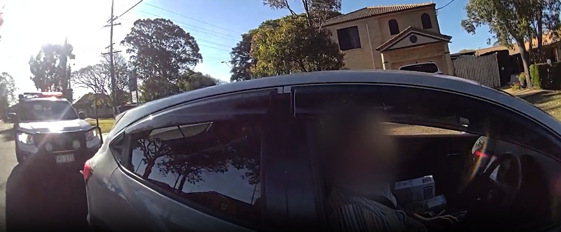 A video still of the side of a dark car, the driver's face blurred.