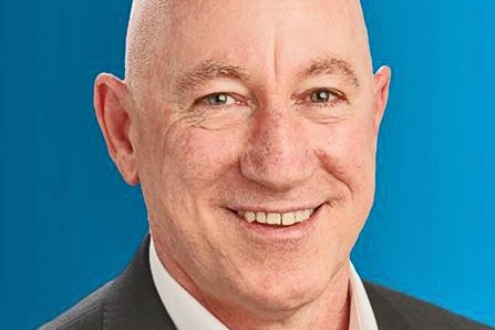 A headshot of a bald man smiling broadly, wearing a blazer and a business shirt.