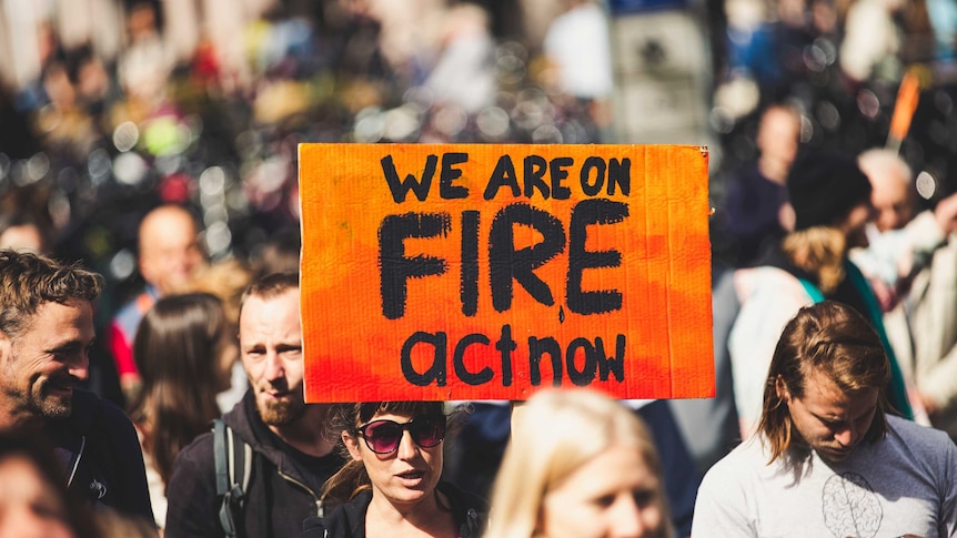 Woman holding a sign that signs 'we are on fire act now' at a rally.