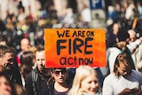Woman holding a sign that signs 'we are on fire act now' at a rally.