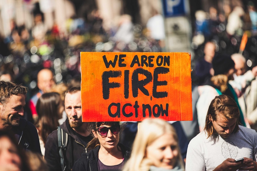 Woman holding a sign that signs 'we are on fire act now' at a rally.