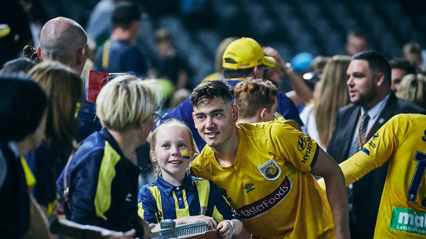 A soccer player smiles at fan taking a photo alongside a smiling young female fan