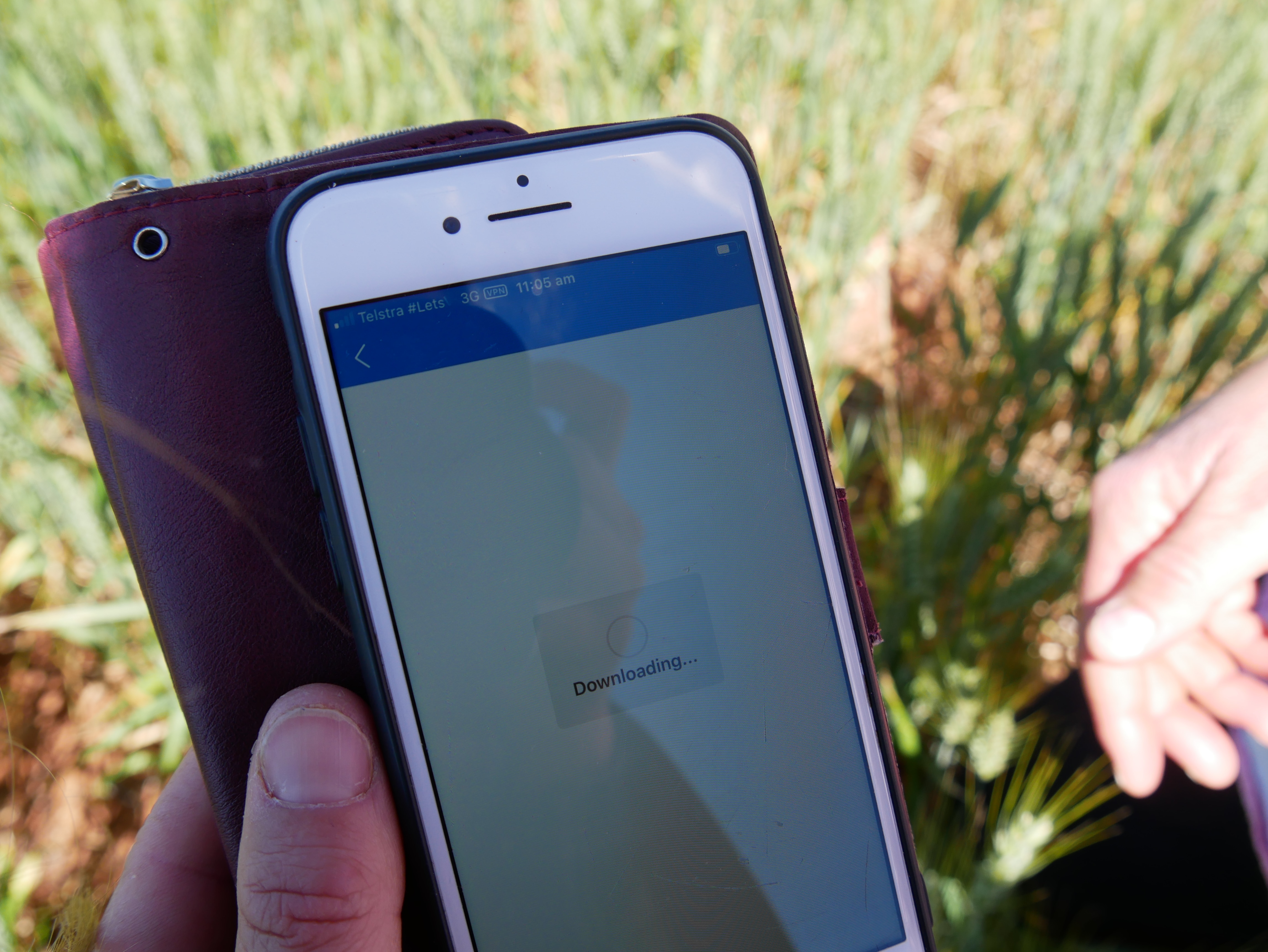 A hand holds a phone which shows a downloading sign, and one bar of 3G signal.