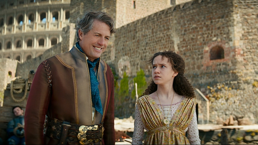 Middle-aged white man with dark hair and young white girl with curly brown hair walk outside a castle dressed in medieval garb.