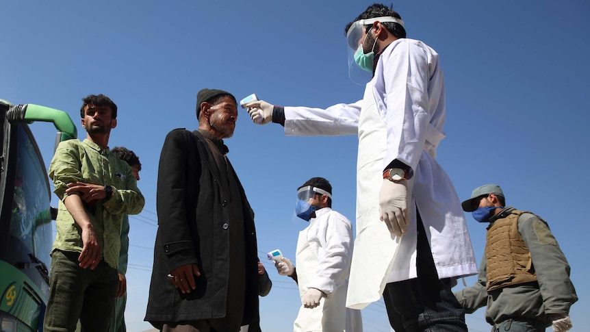 Health workers measure the temperature with a heat gun of Afghan passengers by a road side.