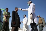Health workers measure the temperature with a heat gun of Afghan passengers by a road side.