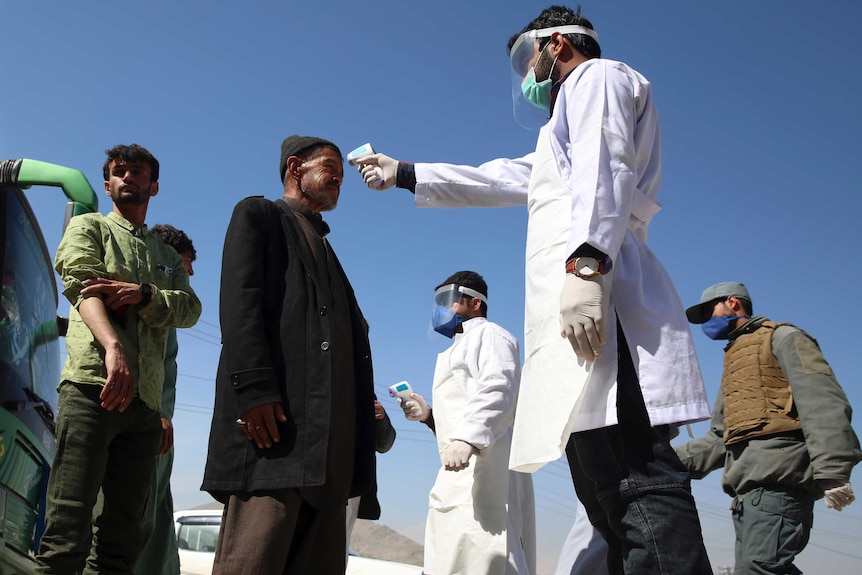Health workers measure the temperature with a heat gun of Afghan passengers by a road side.