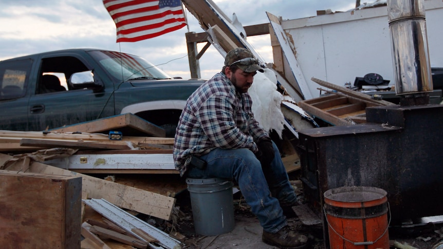 Josh Cox stays warm as he sits next to a wood stove in the remains of his home on March 3, 2012 in Chelsea, Indiana.