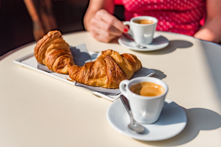 Two croissants and two short espresso coffees sitting on a cafe table