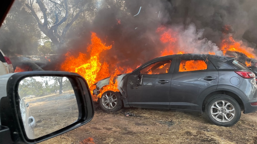 A small hatchback car on fire in a carpark.