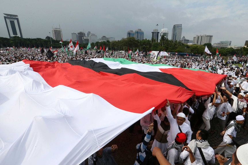 A crowd of people holding large Indonesian and Palestinian flags above their heads.