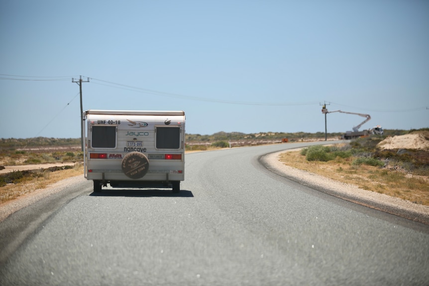 A caravan pictured from behind driving past a power line and sand plains.